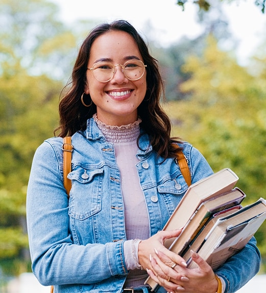 Smiling young college student holding books on campus