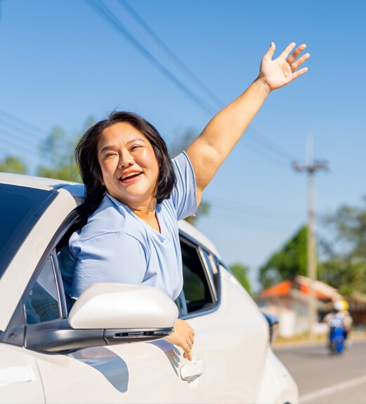 Woman waving out from her driver's side window of her car
