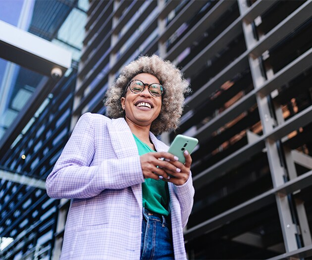 Smiling woman holding her phone outside an office building