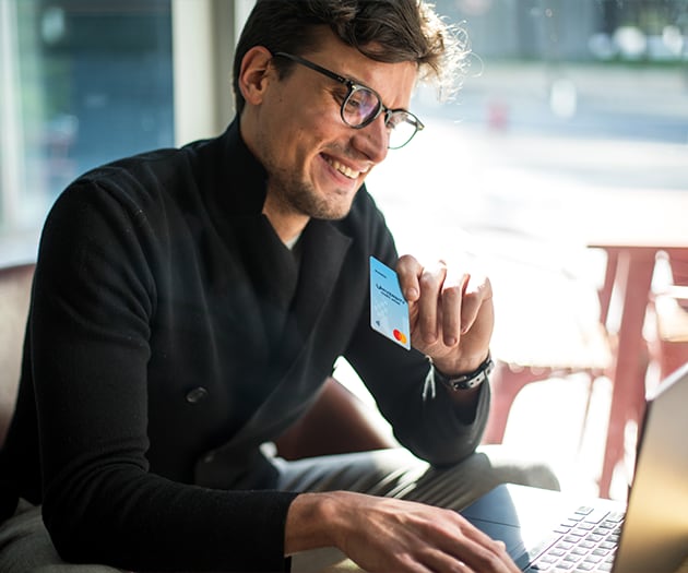 Young man making on online purchase at his laptop while holding a UCU Business Credit Card