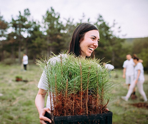 Young woman smiling carrying a bundle of young trees to plant and support the environment