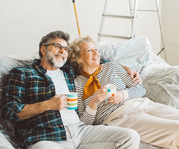 Middle aged couple sitting on a couch looking up at their home improvement project