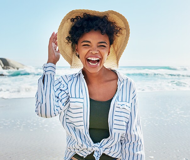 Smiling young woman holding her hat on the beach