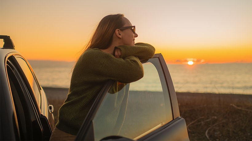 Woman parked car on the beach watching the sunset