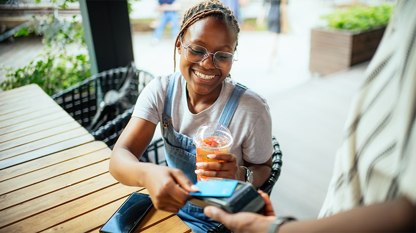 Smiling young woman taps her card to pay at a restaurant