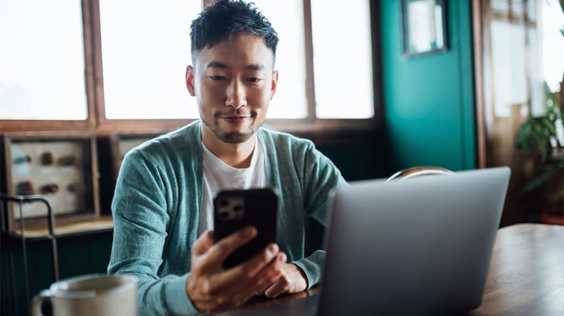 Smiling young man looking at his phone and making a money transfer