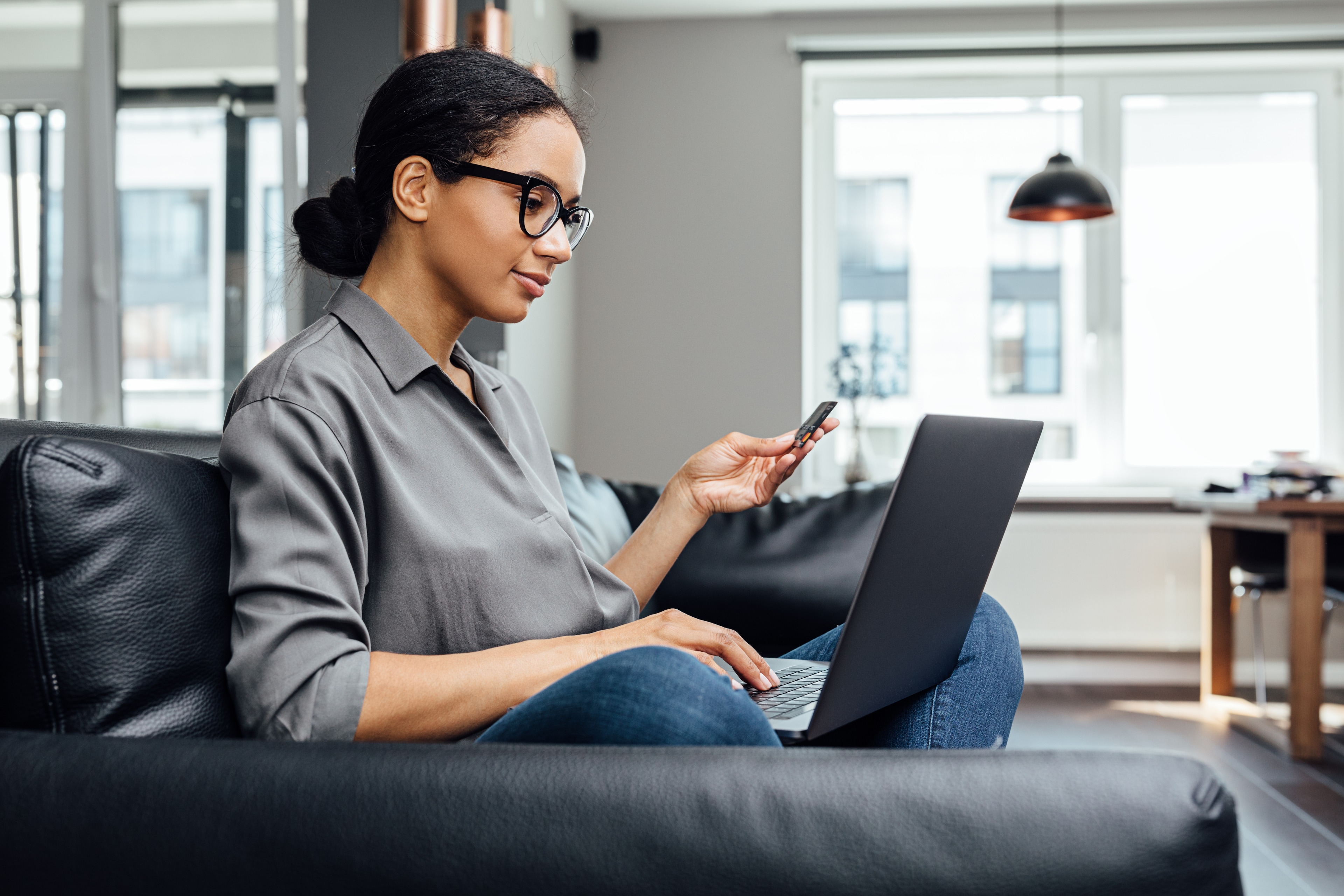 A woman sitting on a couch using a laptop and a phone