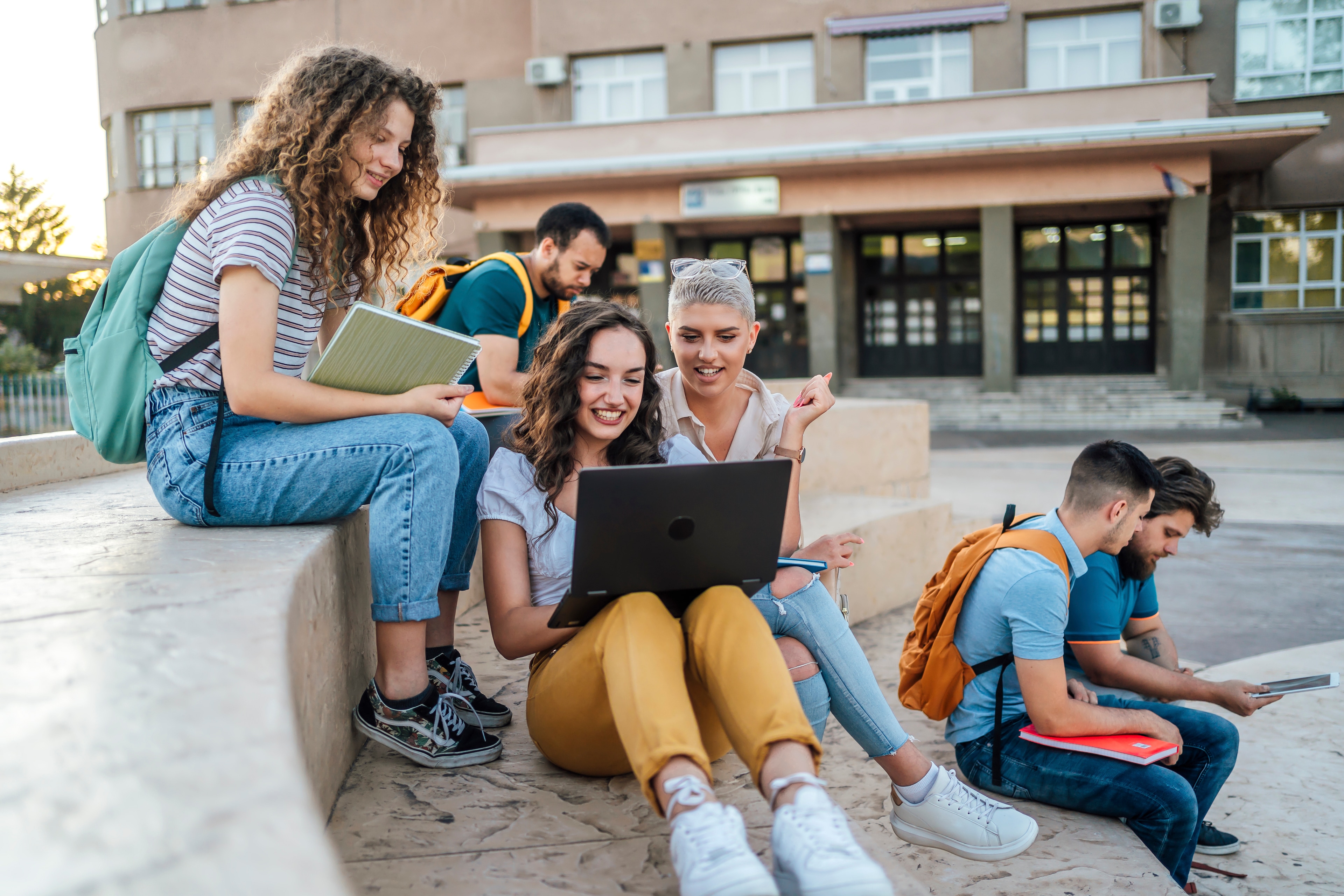 A group of people sitting on a ledge looking at a laptop
