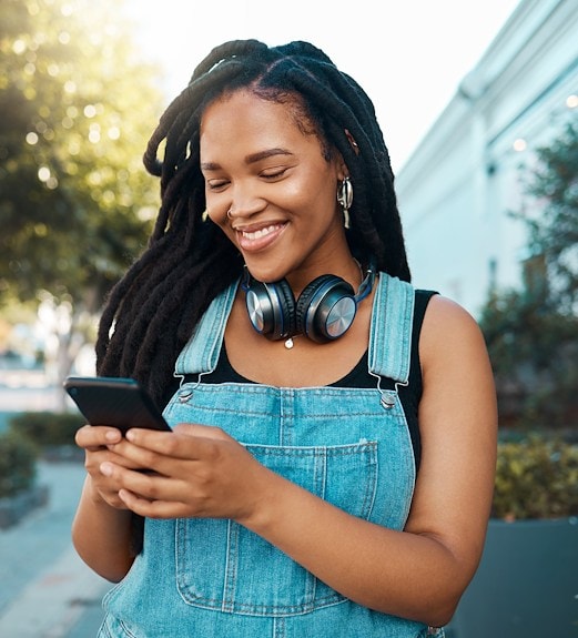A smiling woman looking down at the smart phone in her hands