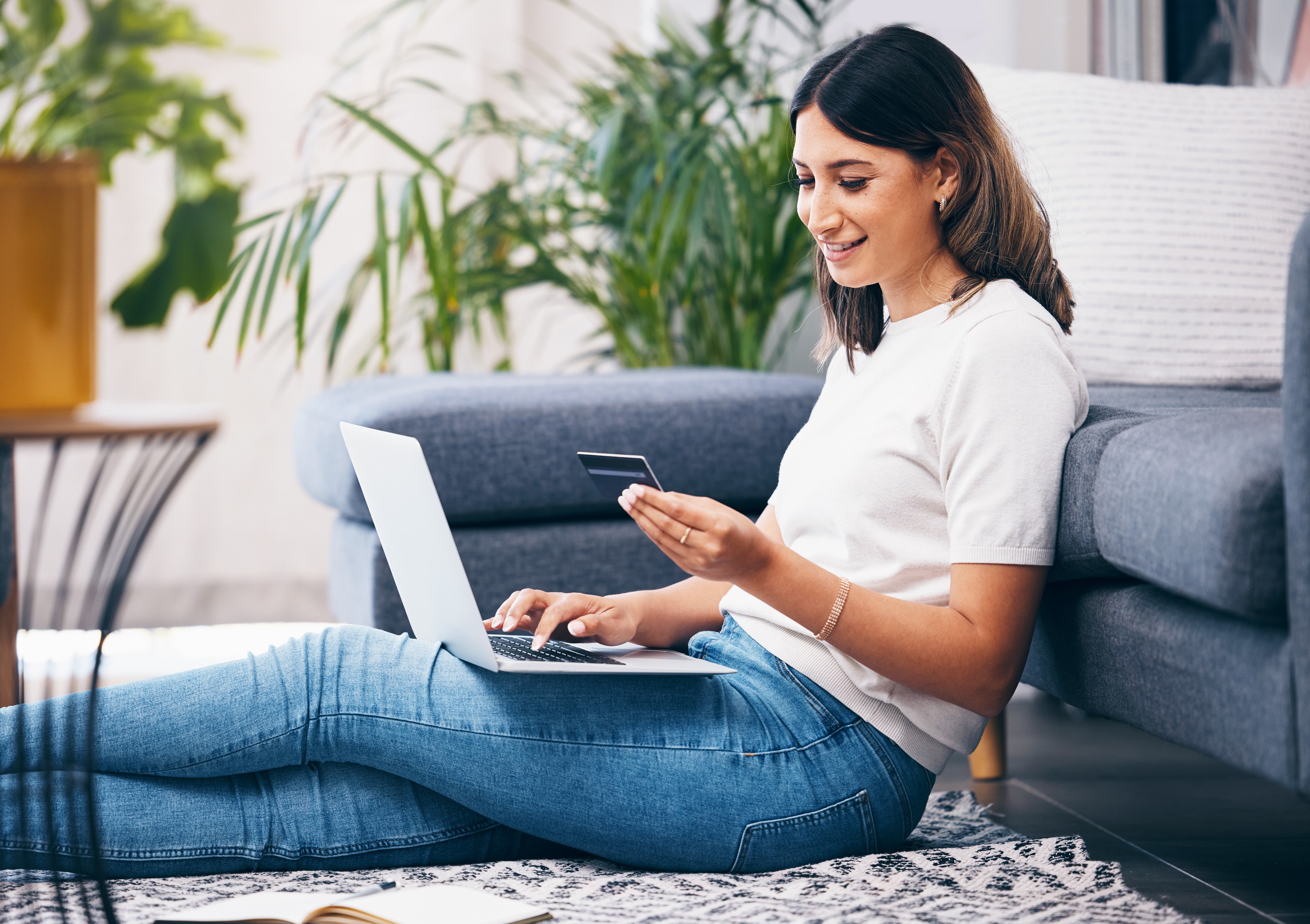 A woman sitting on the floor with a laptop and a credit card