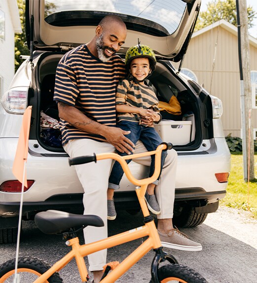 A father holding his young child in front of the car that he refinanced