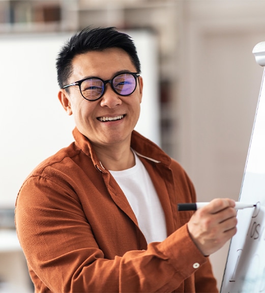 Smiling man wearing glasses writing on a whiteboard