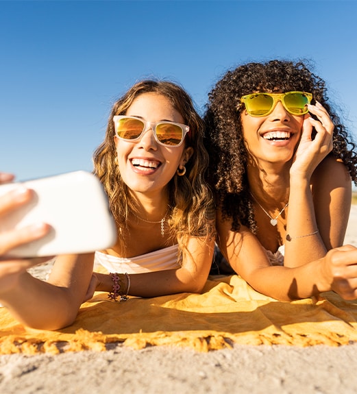 Two friends wearing sunglasses taking a selfie together on the beach