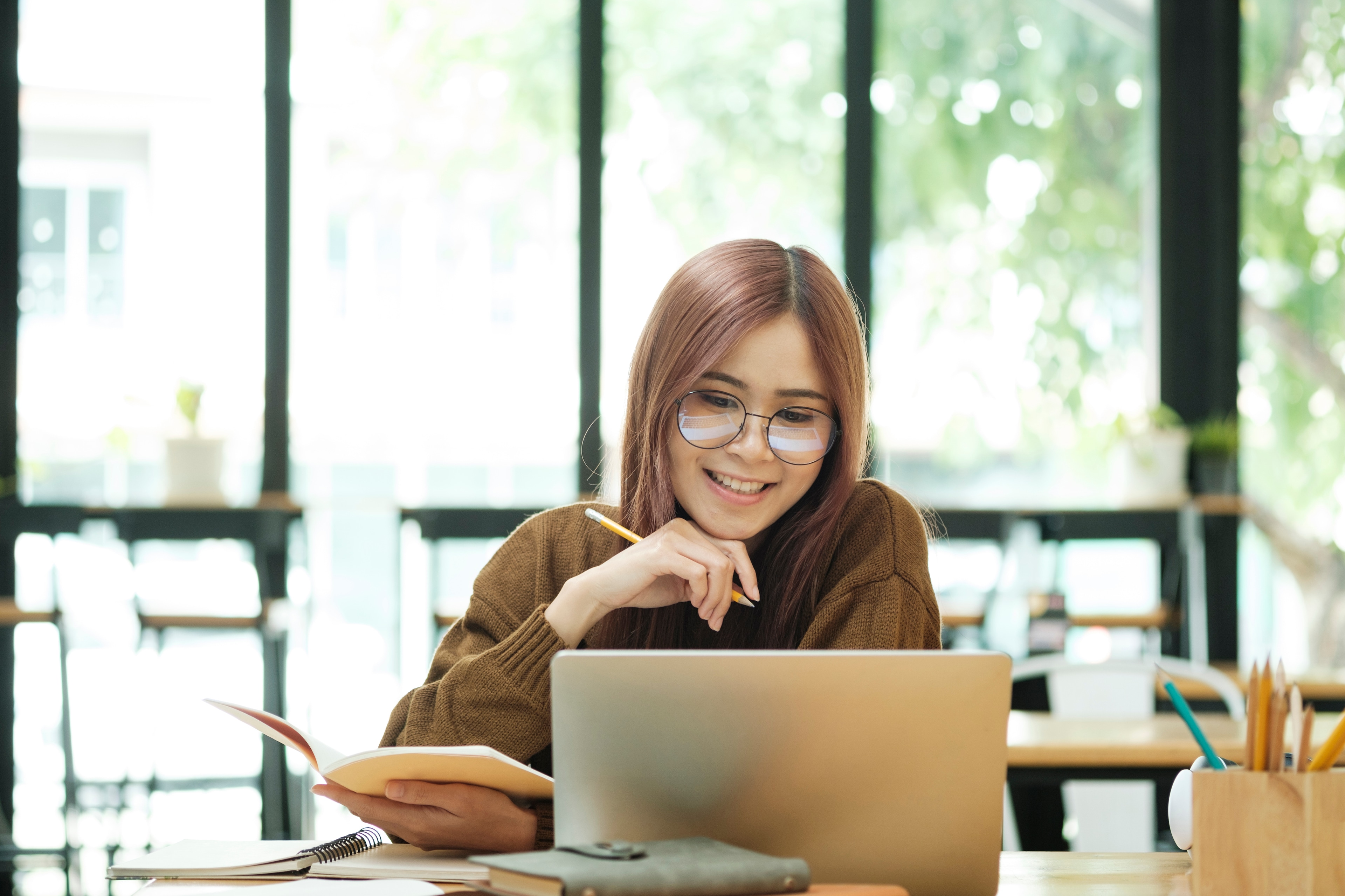 A woman sitting at a table with a laptop and a pencil in her hand