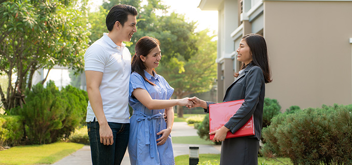 Couple shaking hands with a real estate agent outside a home