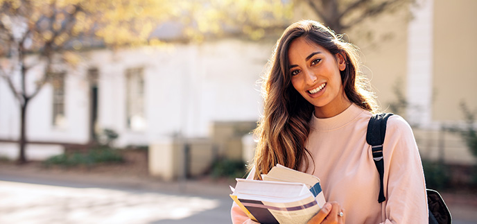 College student holding books and a backpack on campus