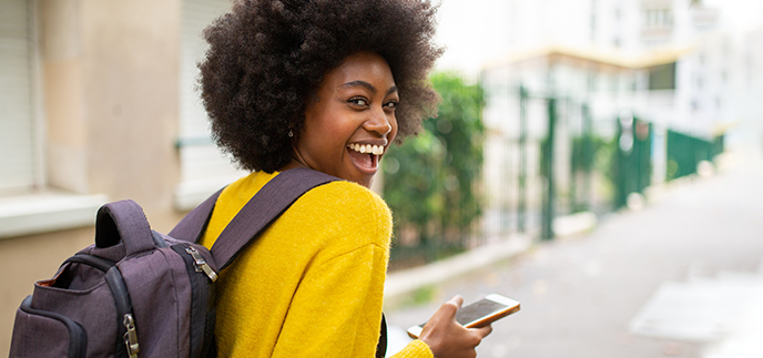 Student walking outside holding her backpack and phone