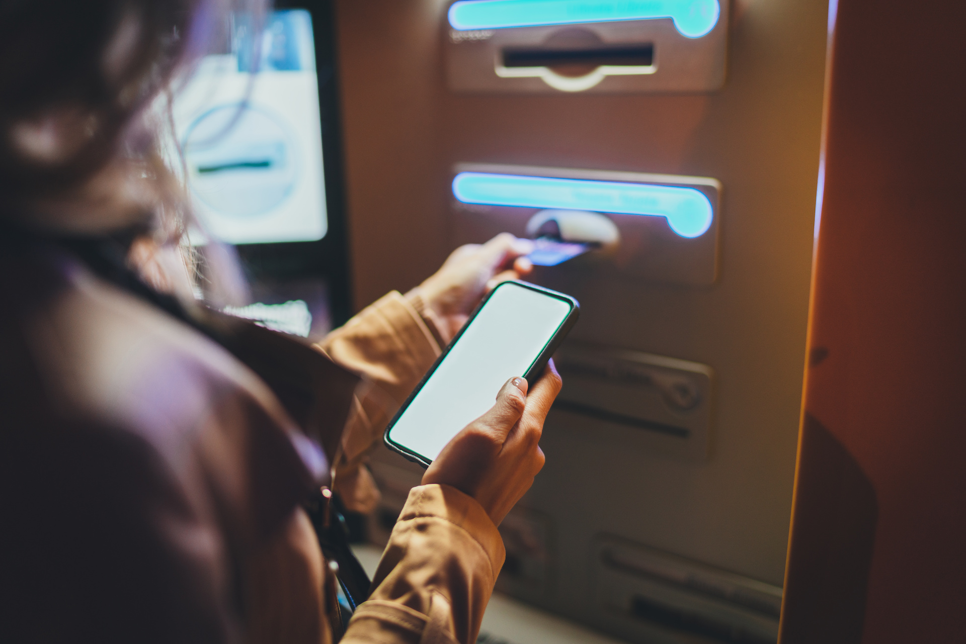 Close up view of hand holding phone at an ATM console